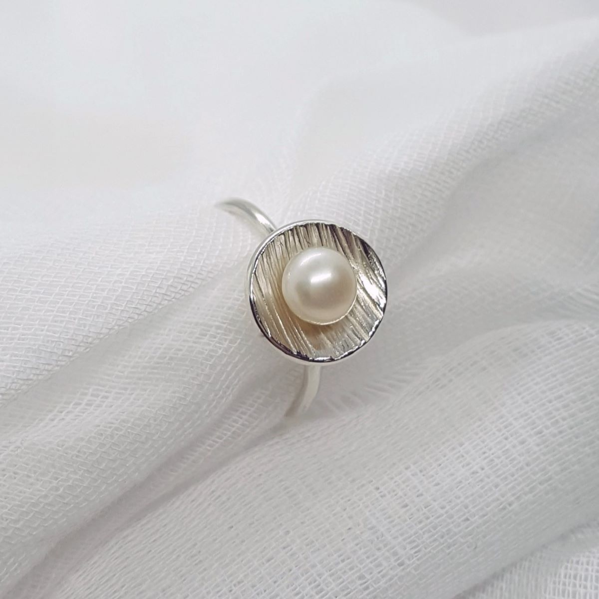 white button freshwater pearl set in a textured silver cup ring
