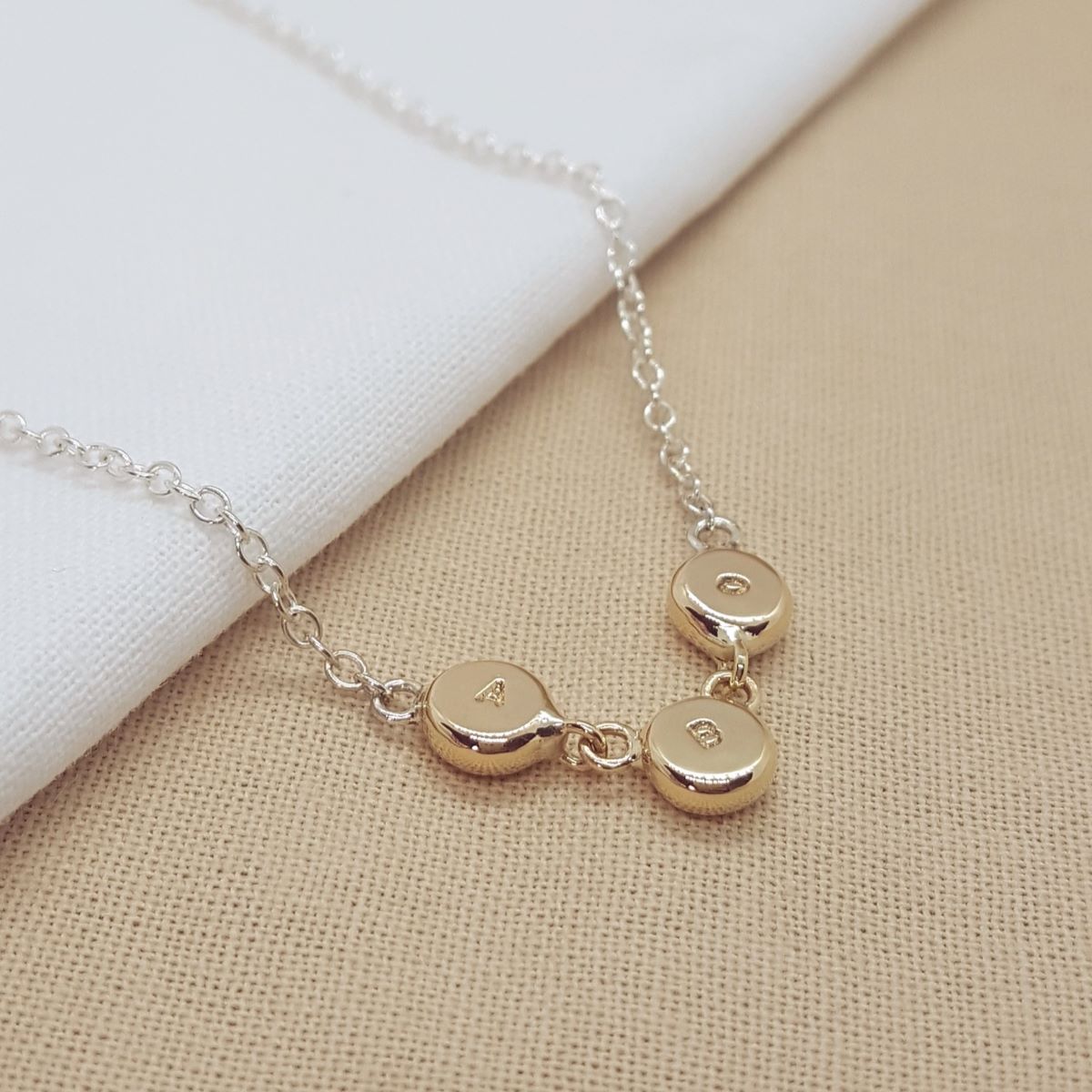 three 9ct yellow gold discs hand stamped with initials and connected with jump rings, hanging on a silver trace chain