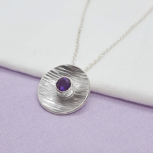 5mm round faceted amethyst set in a large textured silver disc and hanging on a silver trace chain. Handmade in Kent.