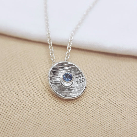 round faceted aquamarine set in a textured silver cup, hanging from a silver trace chain. Handmade in Marden, Kent.