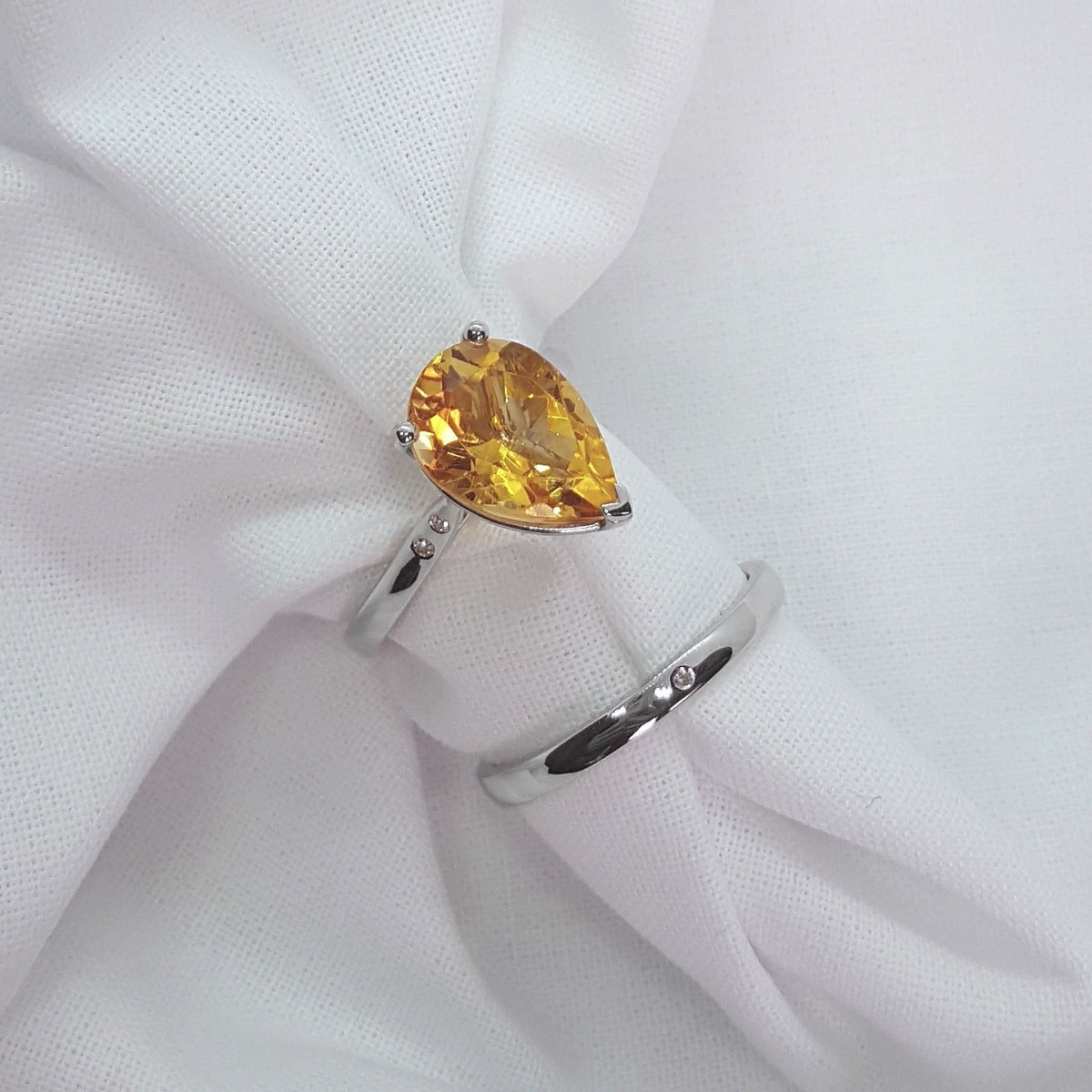 Silver ring with a yellow gemstone on a white fabric background