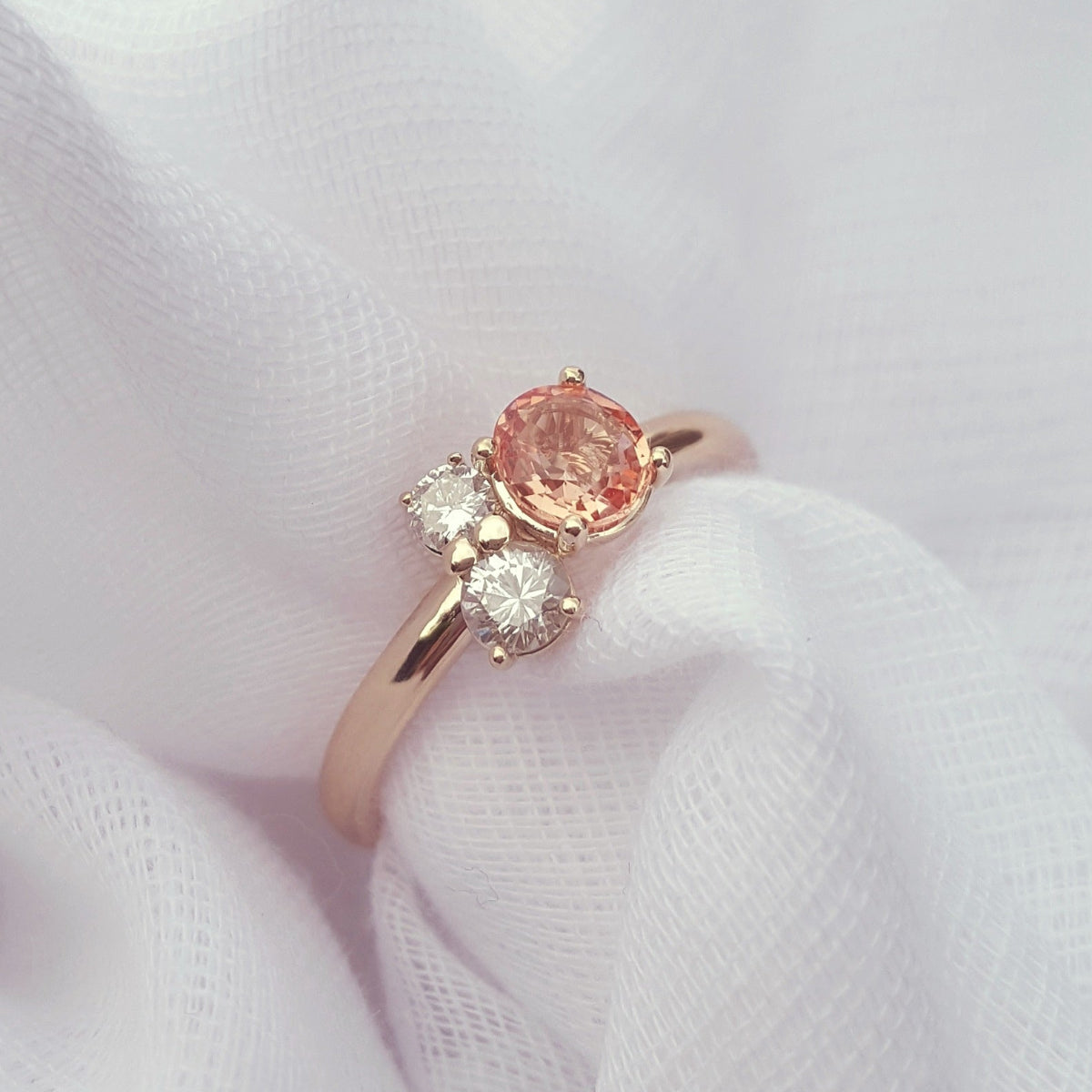 Rose gold ring with a pink gemstone and smaller diamonds on a white fabric background