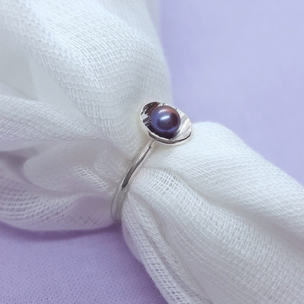 peacock coloured freshwater pearl set in a silver textured cup, silver wire band, handmade jewellery in Kent