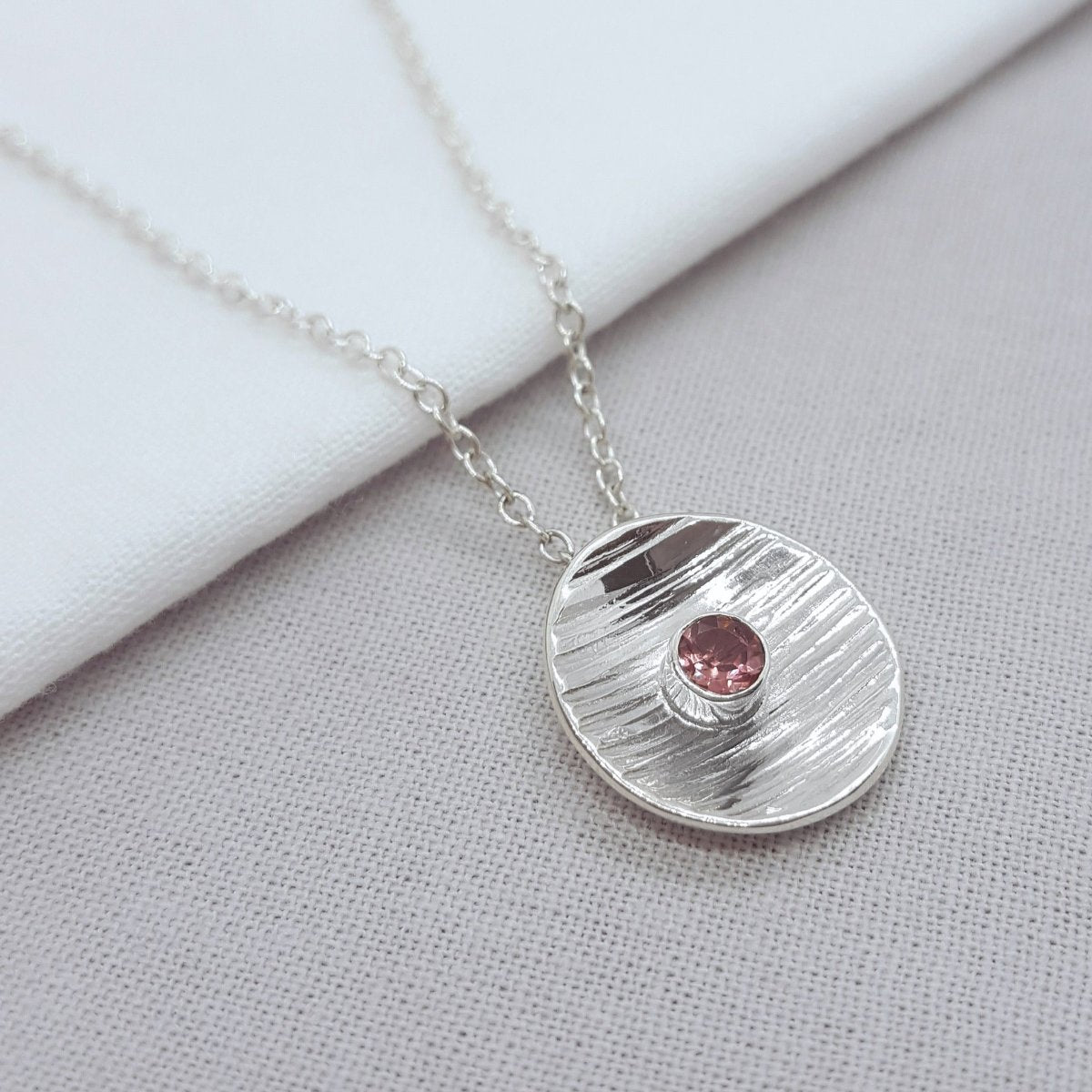 faceted round pink tourmaline tube set in a silver textured disc. Hanging from a trace chain. Handmade in the Kent countryside. 