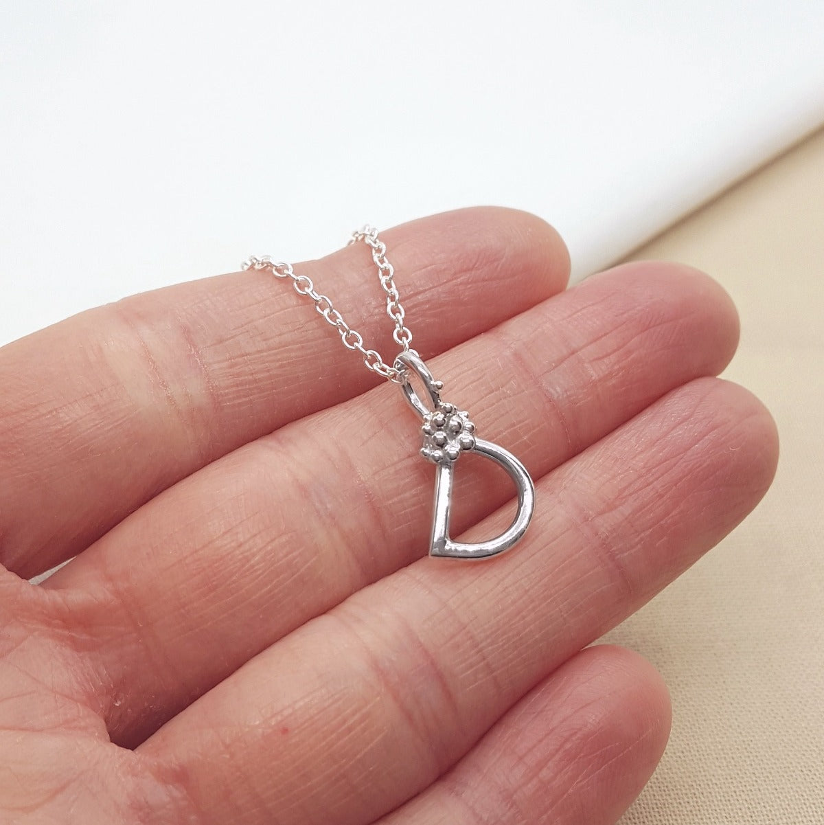 silver handmade initial pendant with granulation detail, hanging on a silver trace chain