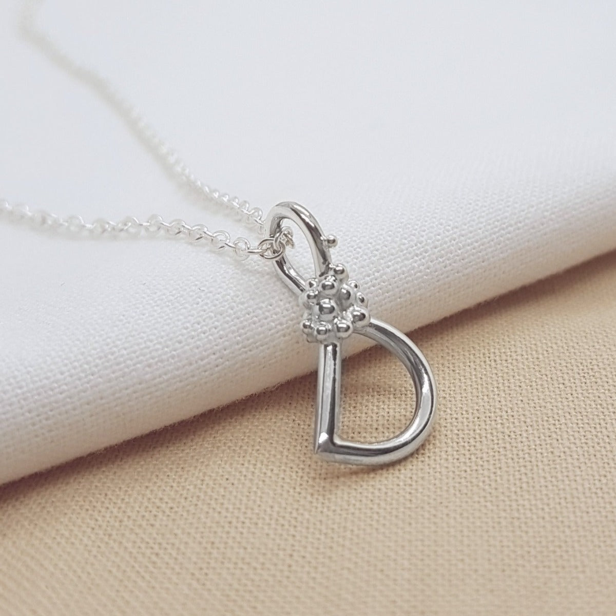 silver handmade initial pendant with granulation detail, hanging on a silver trace chain