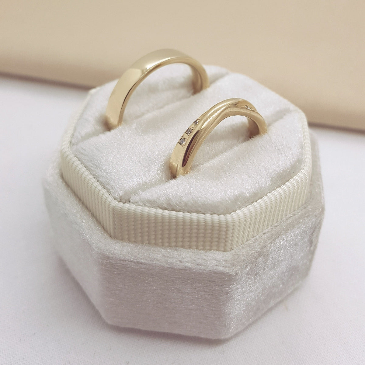 Two gold rings in a hexagonal white jewelry box on a light background